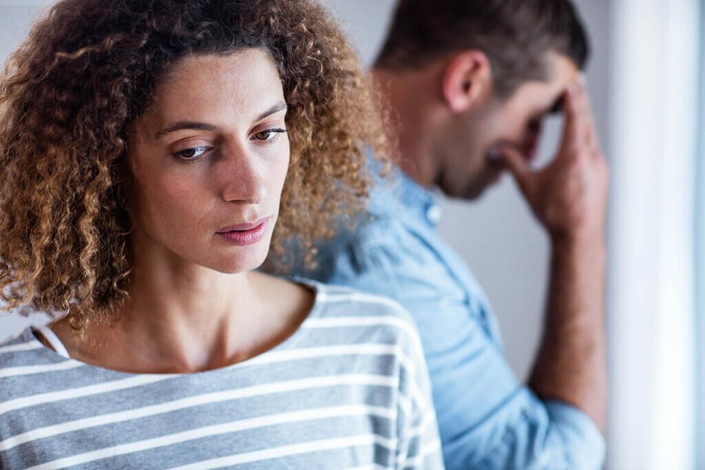 a person holds their head in the background while their partner looks puzzled in the foreground as they struggle with PTSD and relationships